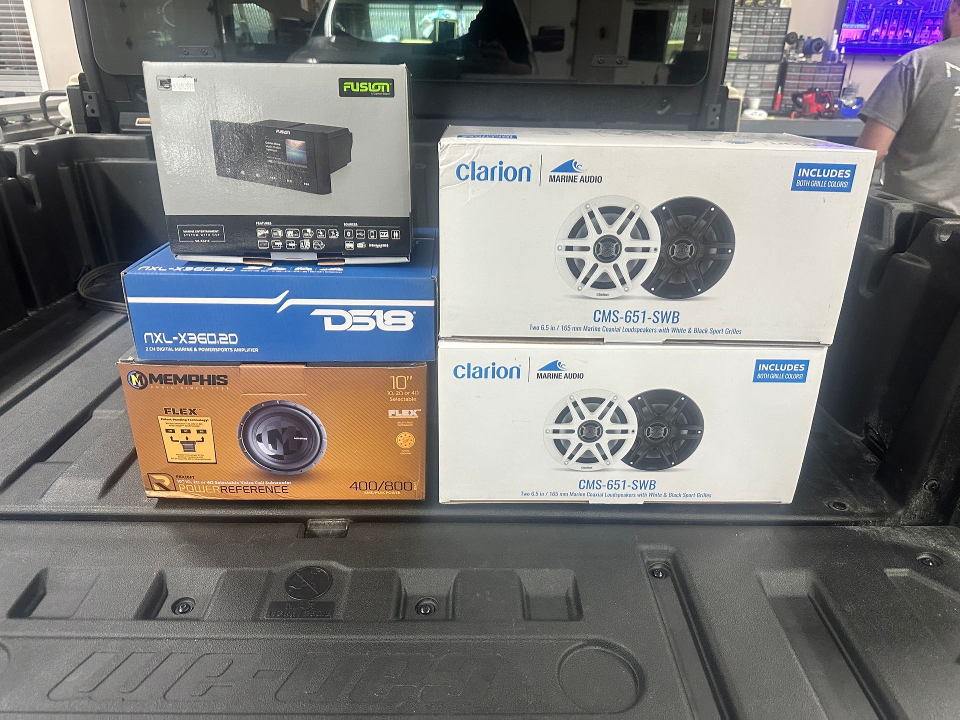 Boxes of car audio equipment stacked in a truck bed, including speakers, a head unit, and amplifier.