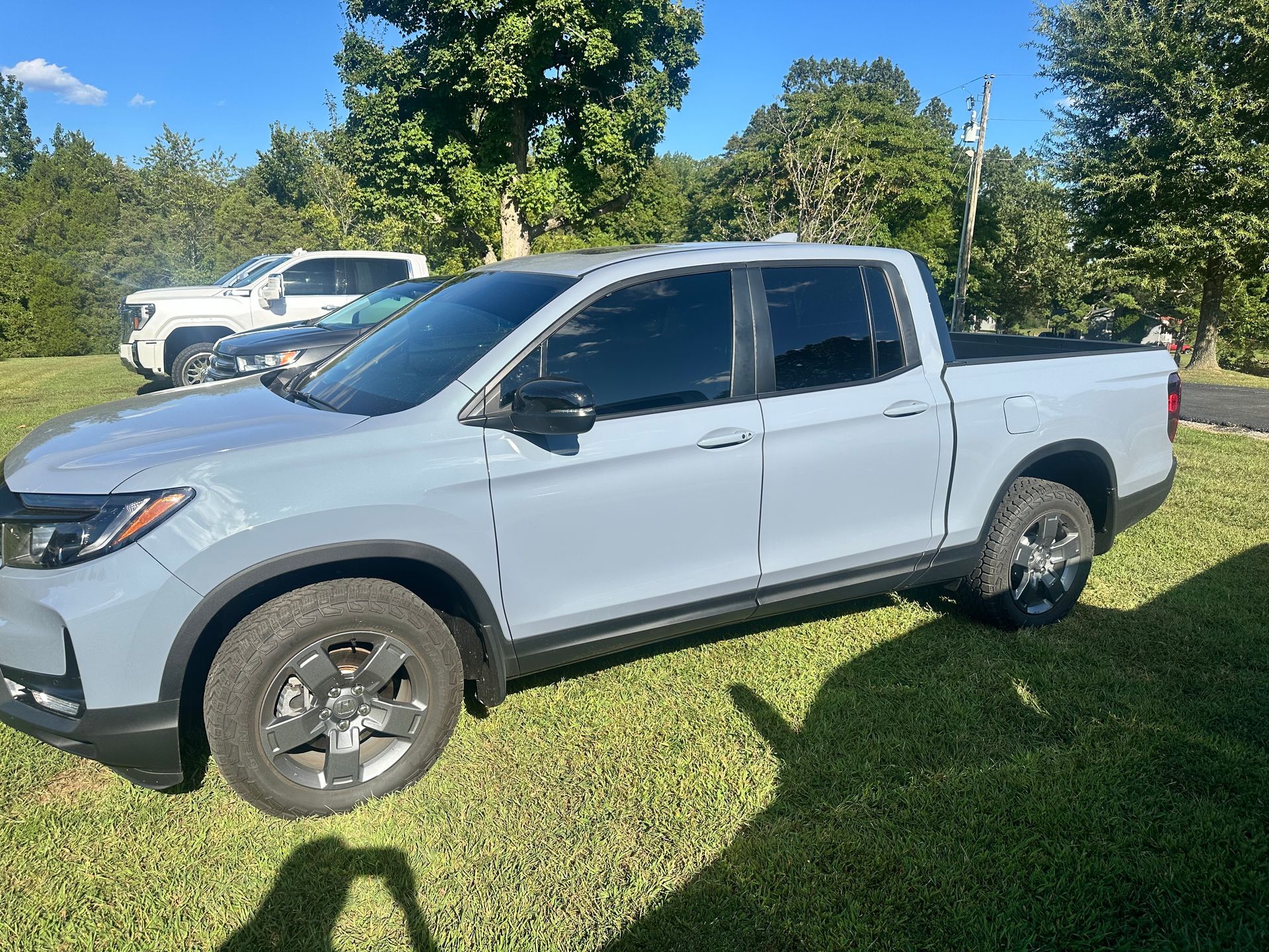 Gray Honda Ridgeline pickup truck parked on grass, sunny day. Other vehicles visible in background.