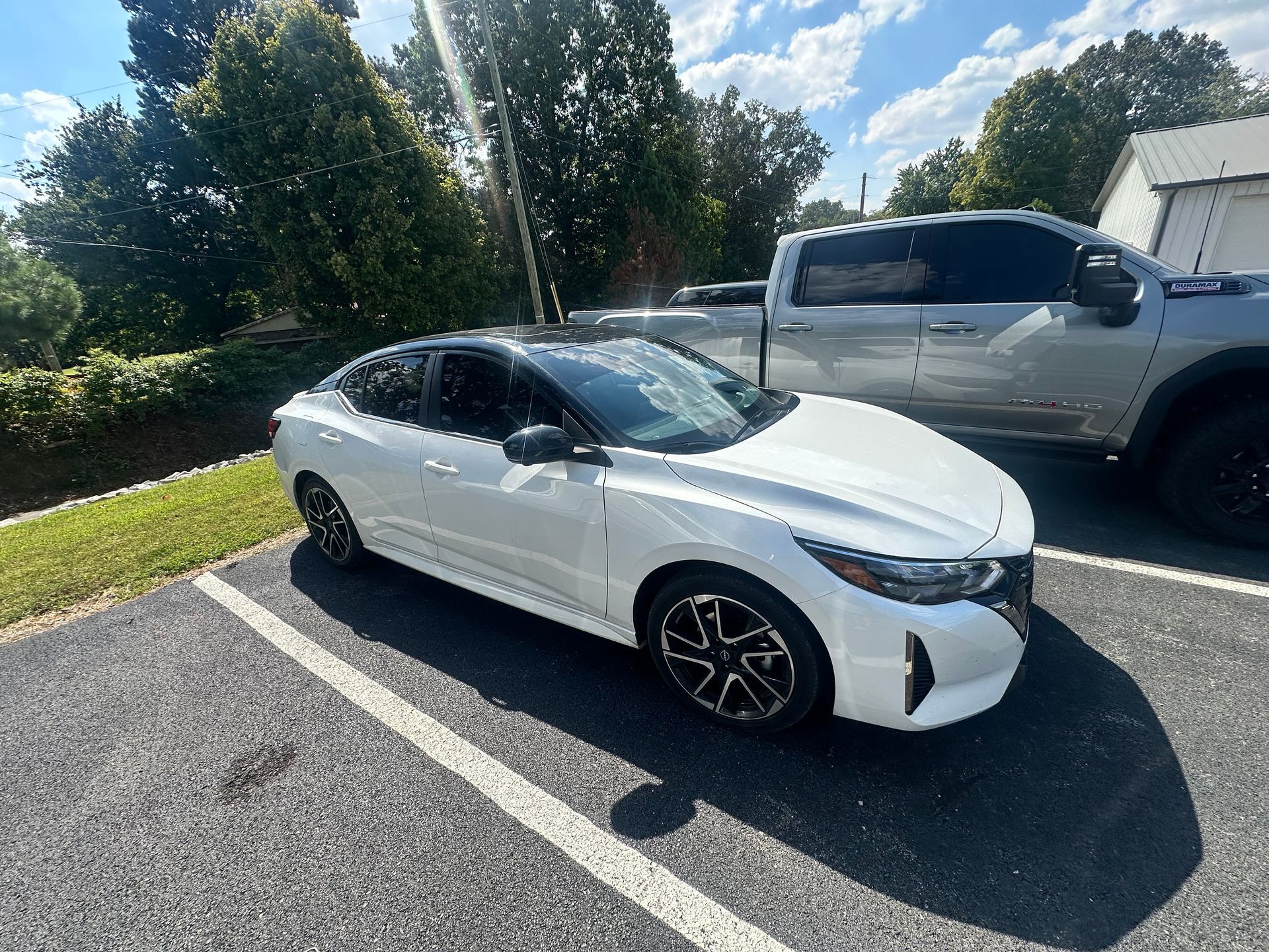 White sedan parked in a parking spot with a black roof next to a silver truck.
