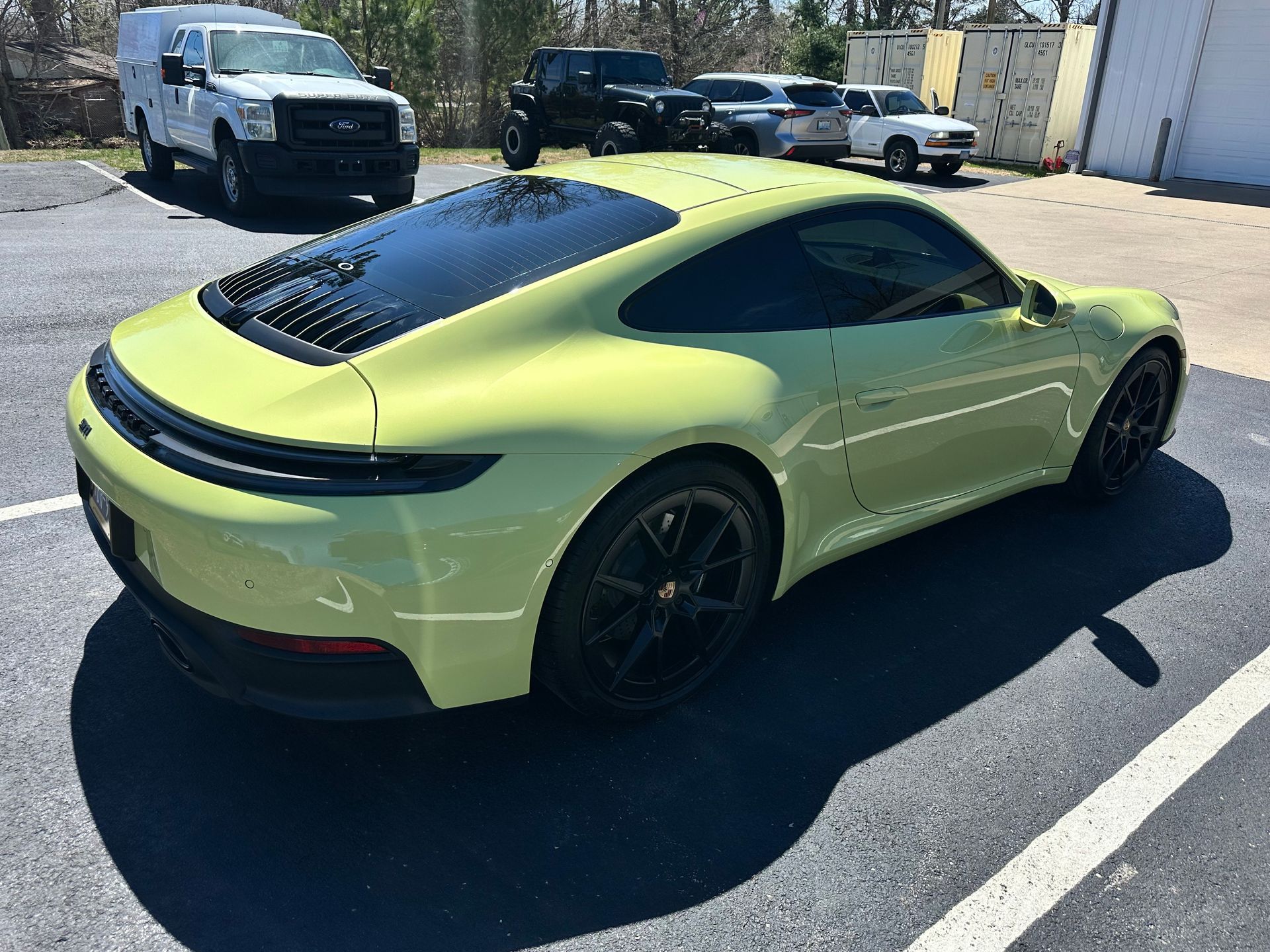 Lime green Porsche coupe parked outside on a sunny day. Black wheels and tinted windows.