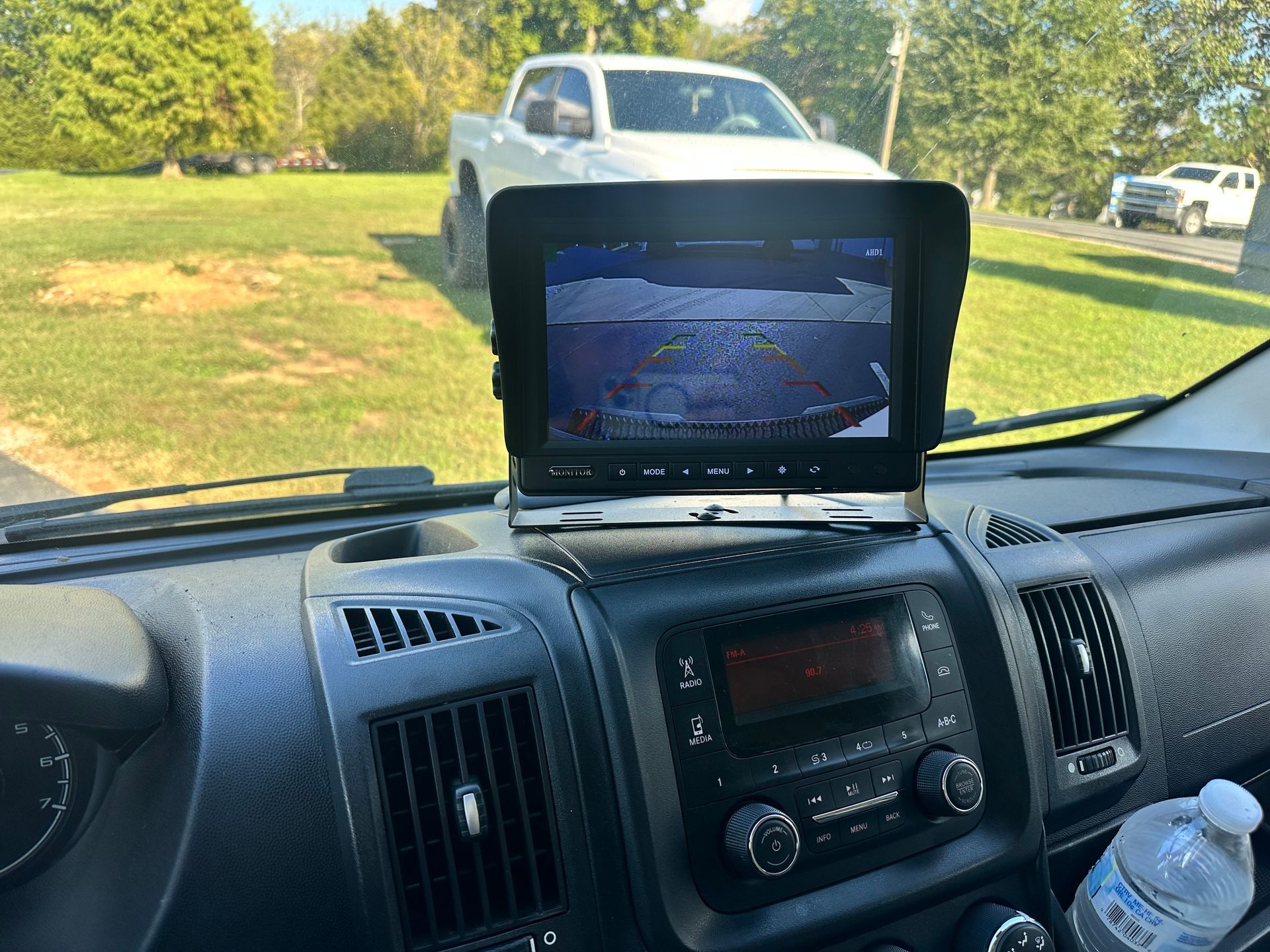 Dashboard view with a backup camera screen displaying a vehicle's rear. A white truck is visible outside.