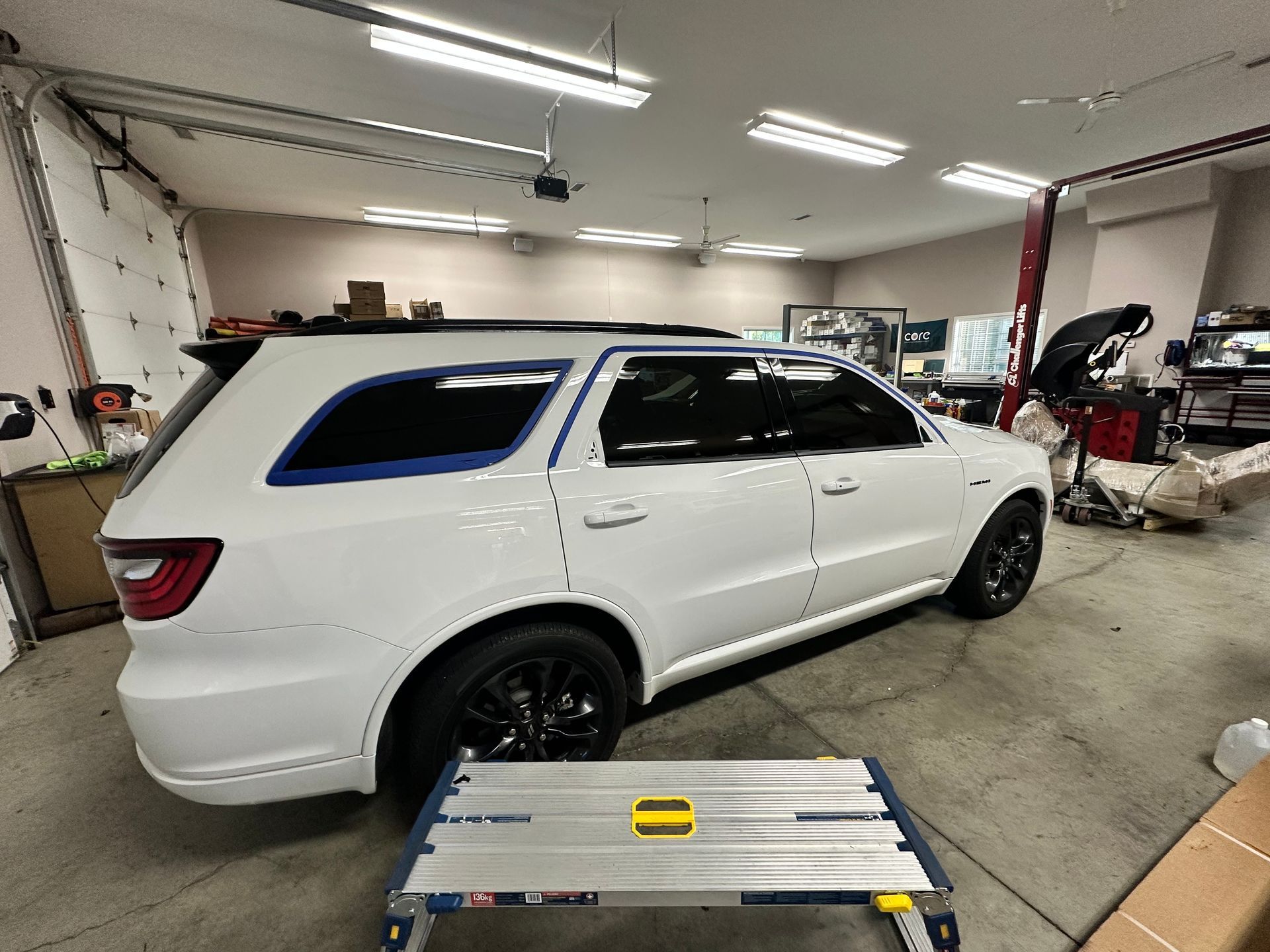 White SUV with black wheels in a garage, window tinting in progress.
