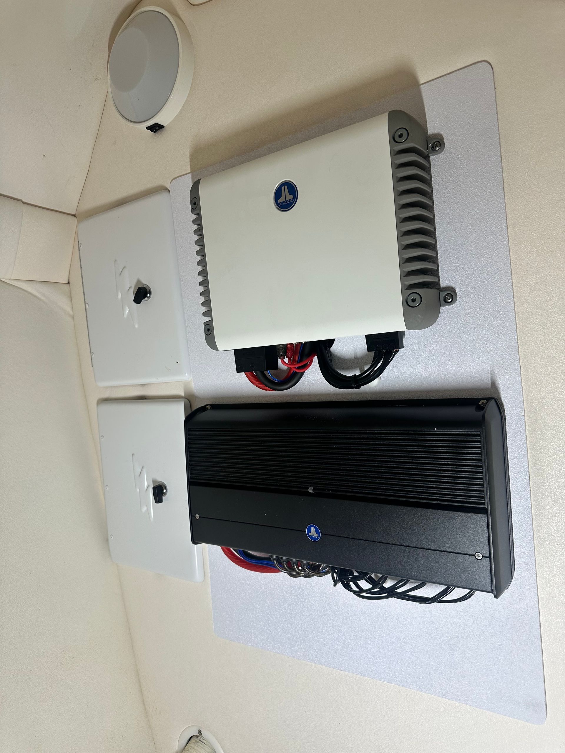 Two boat audio amplifiers, white and black, mounted on white board with speakers.