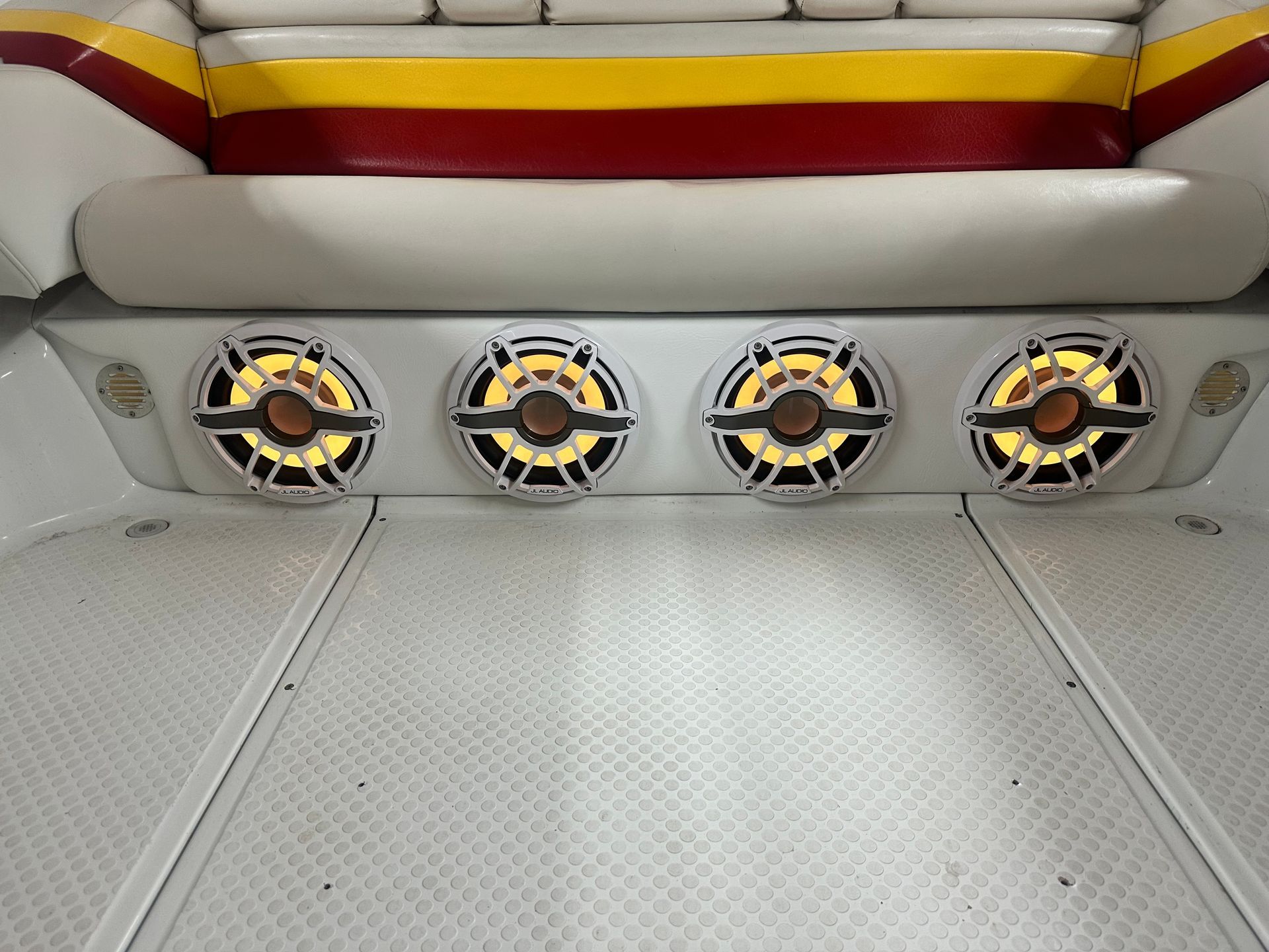 Four lit speakers built into the back of a boat. White deck and red/yellow/white seating.