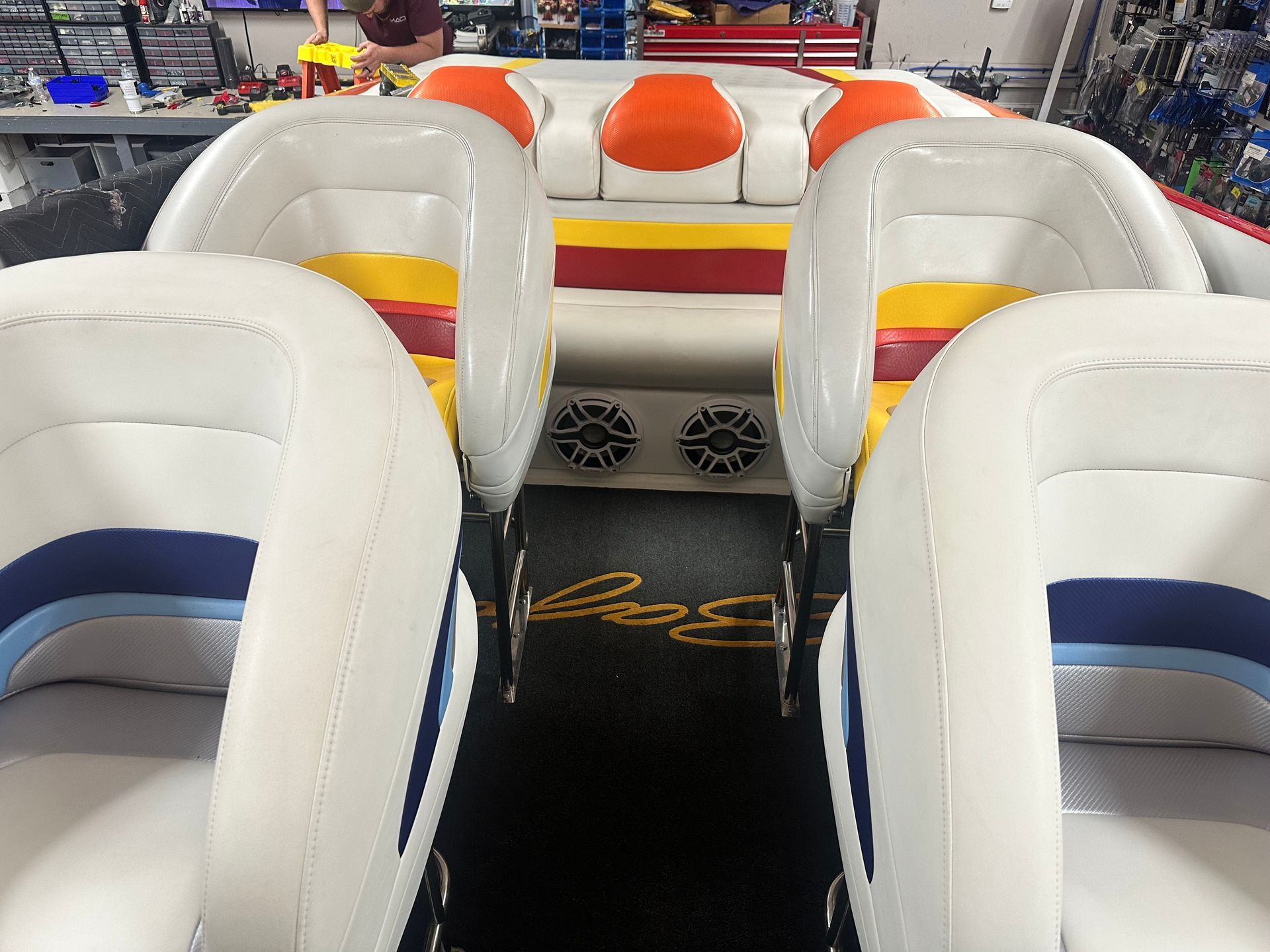 Interior view of a speedboat with white and blue seats, orange and yellow accents, and speakers.