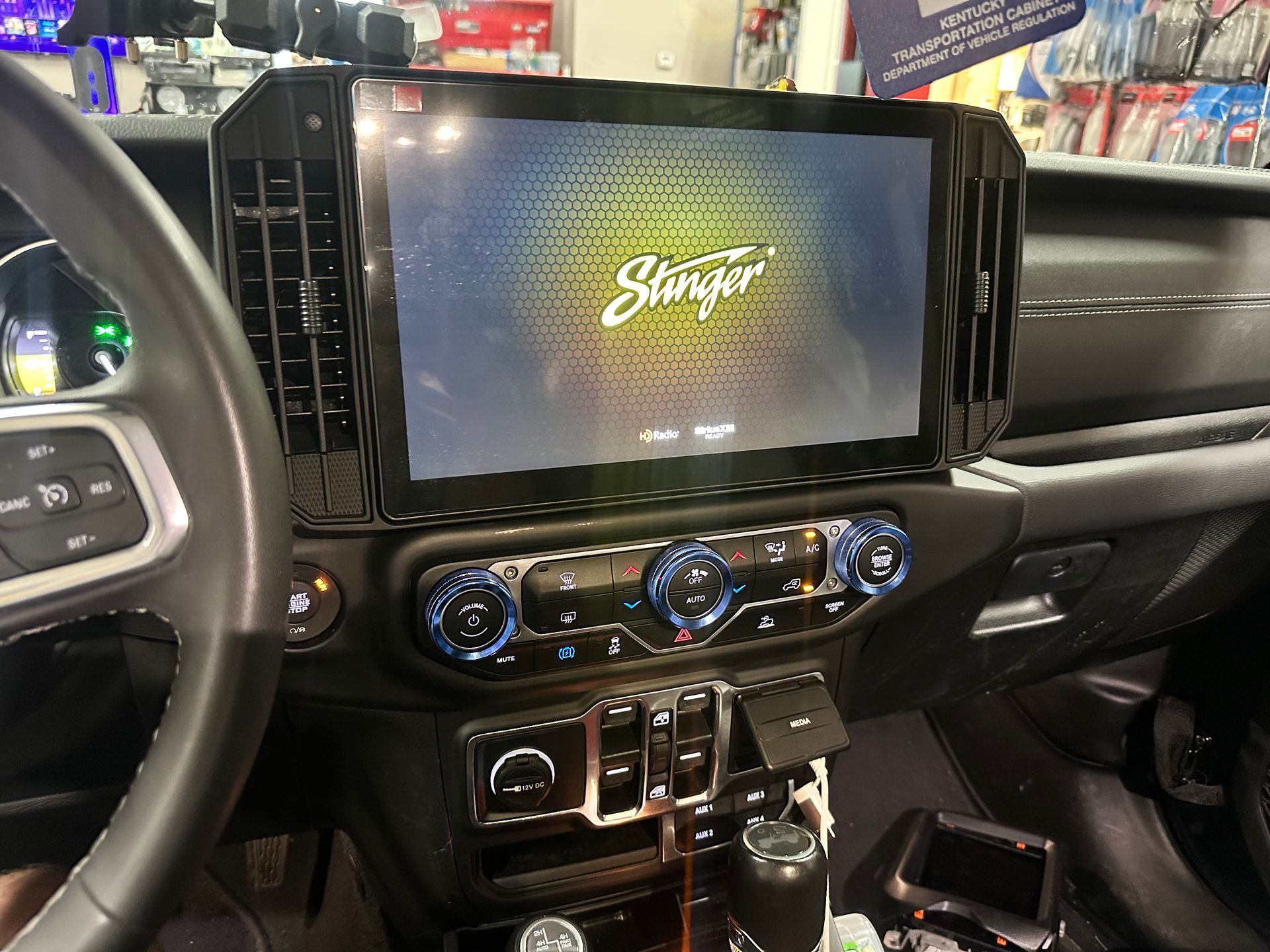 Car dashboard with a large Stinger touchscreen display, blue climate control dials, and black interior.