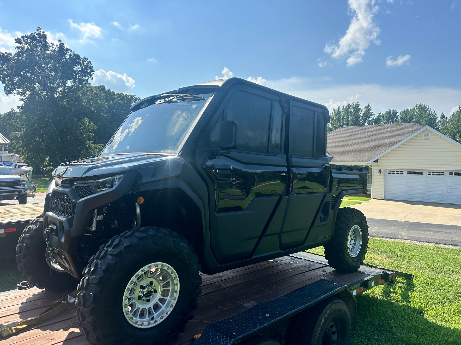 Black, off-road side-by-side vehicle with large tires on a trailer in front of a house.