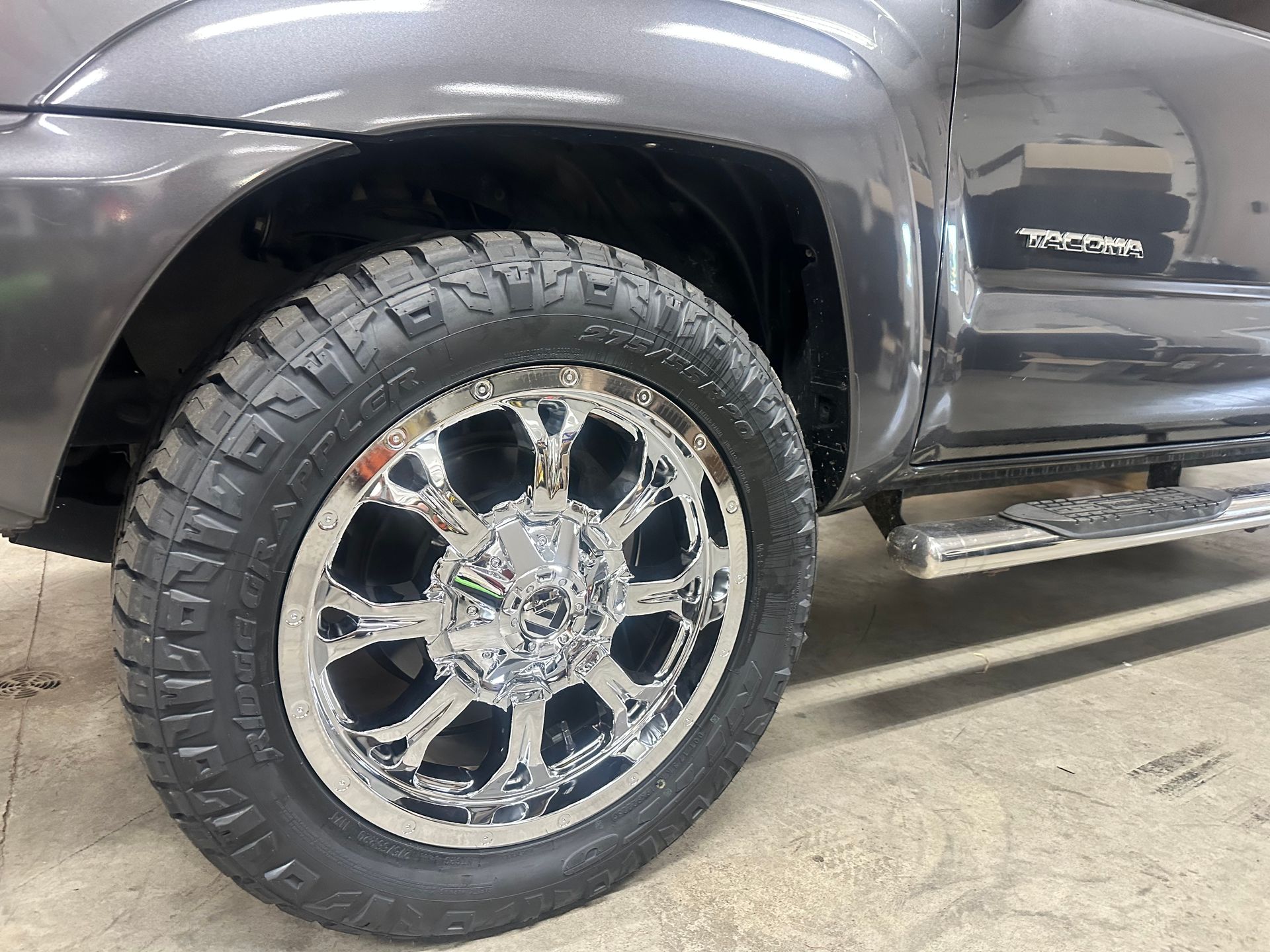 Close-up of a truck's wheel with a chrome rim and off-road tire, gray vehicle, indoor setting.