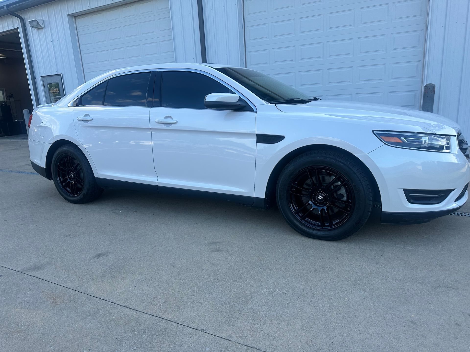 White sedan with black rims parked outside a garage.