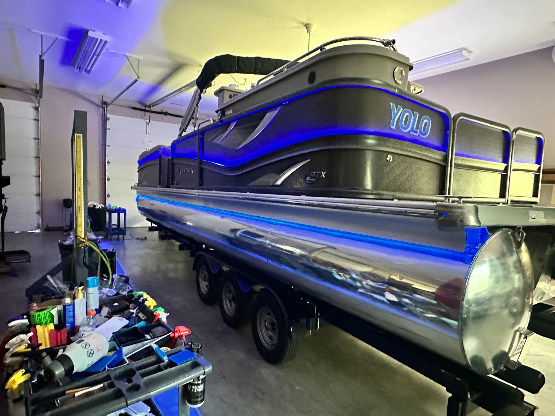 Pontoon boat on trailer, lit with blue and yellow lights inside a garage.