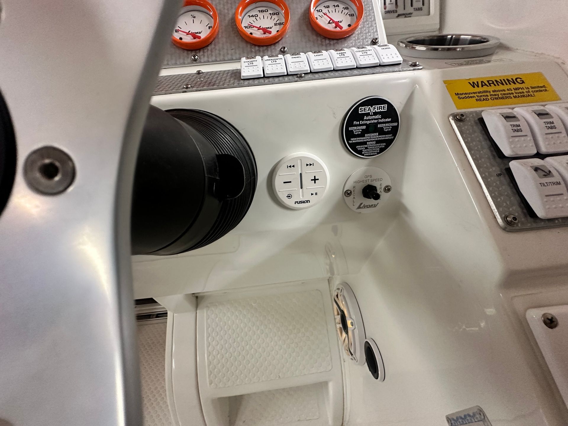 Boat dashboard with gauges, switches, and steering wheel. White interior, orange gauges, black wheel.