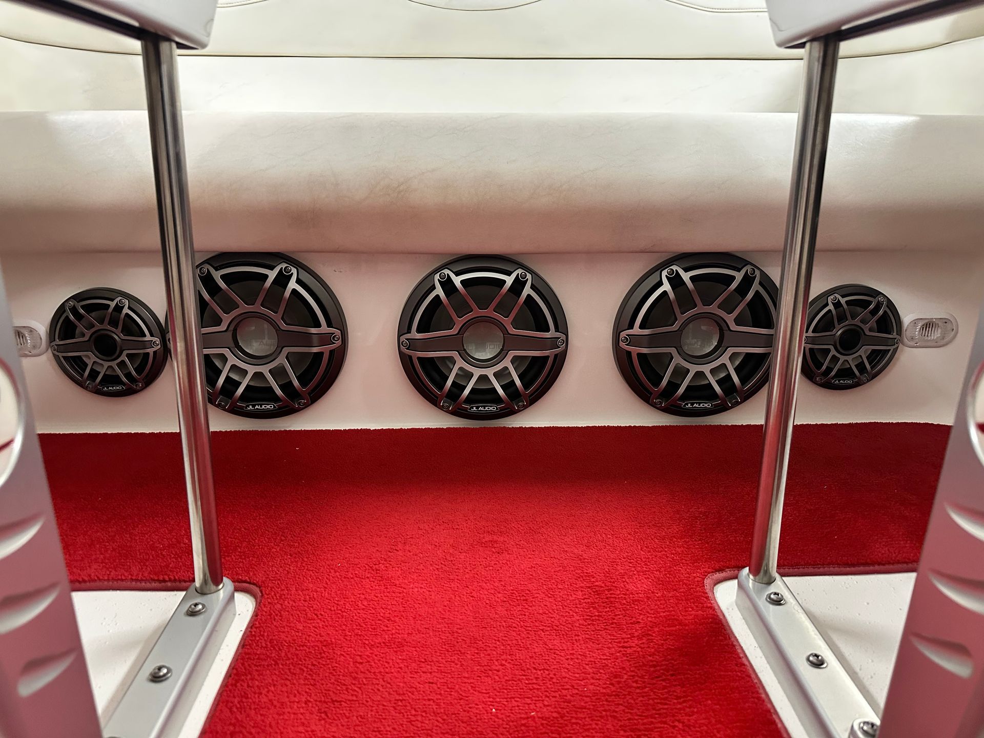 Boat interior with red carpet, white seats, and five speakers.