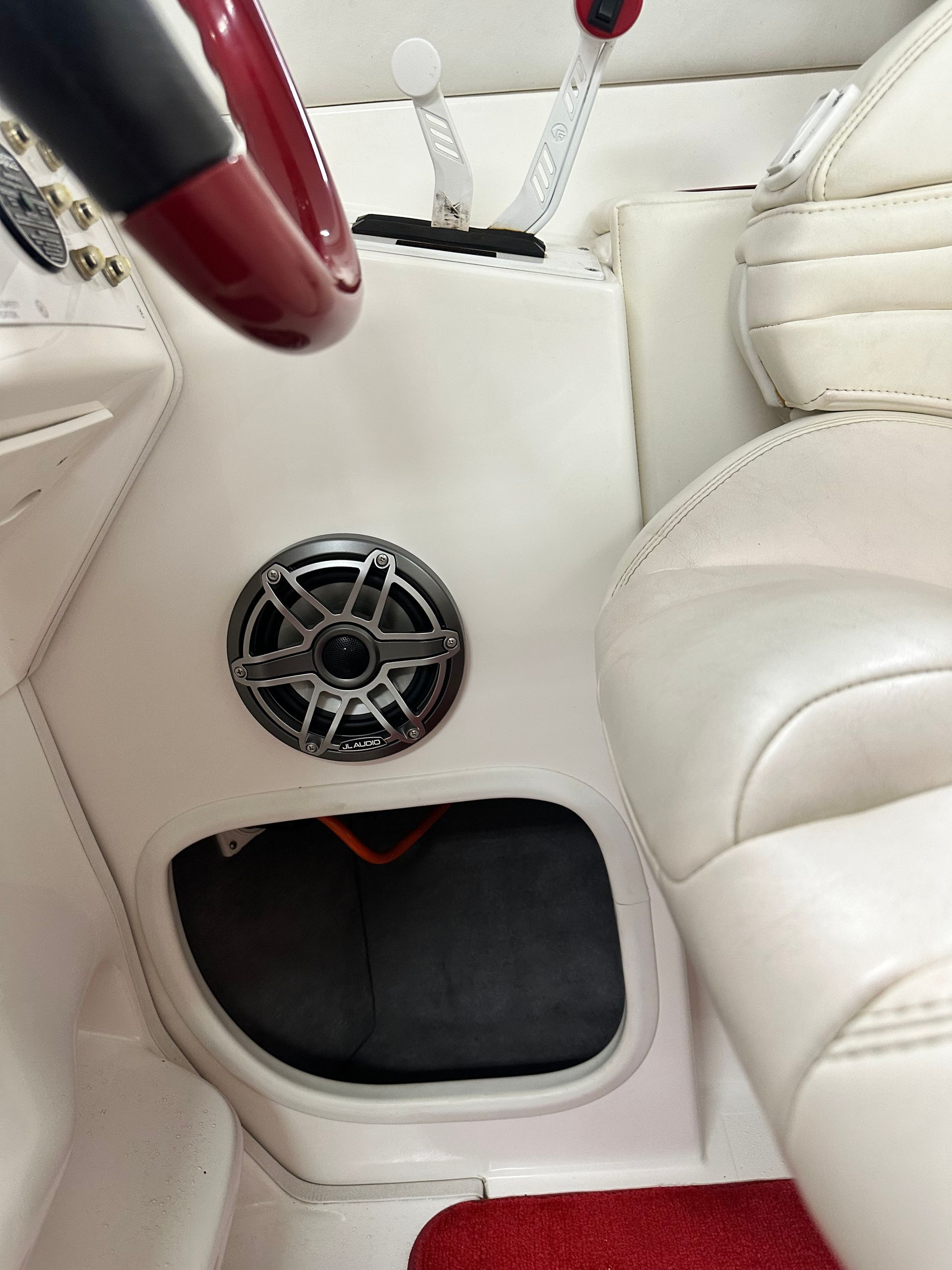 Boat interior with a speaker, white seats, red steering wheel.