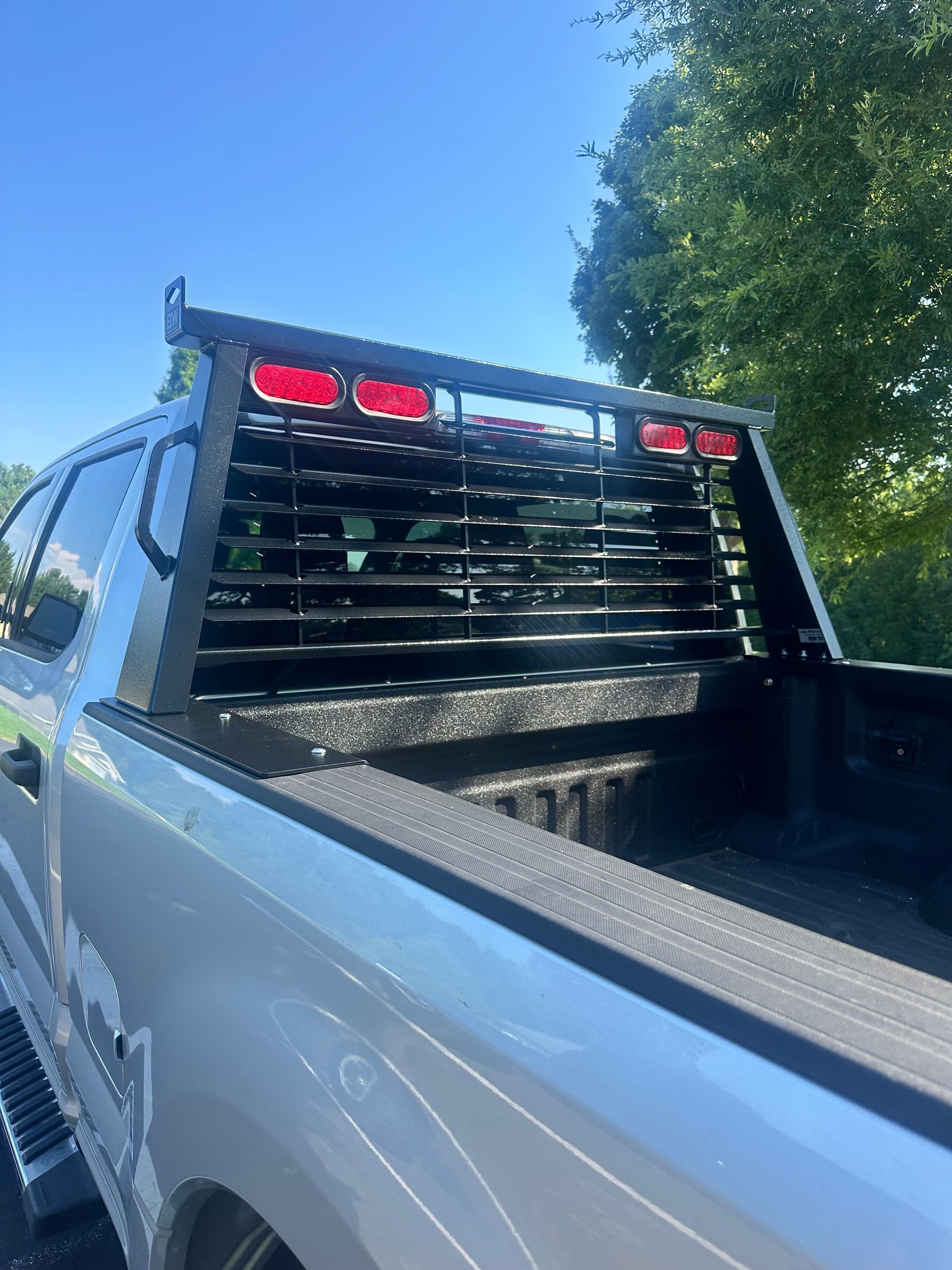 Silver truck bed with black headache rack, red lights, and a sunny outdoor setting.