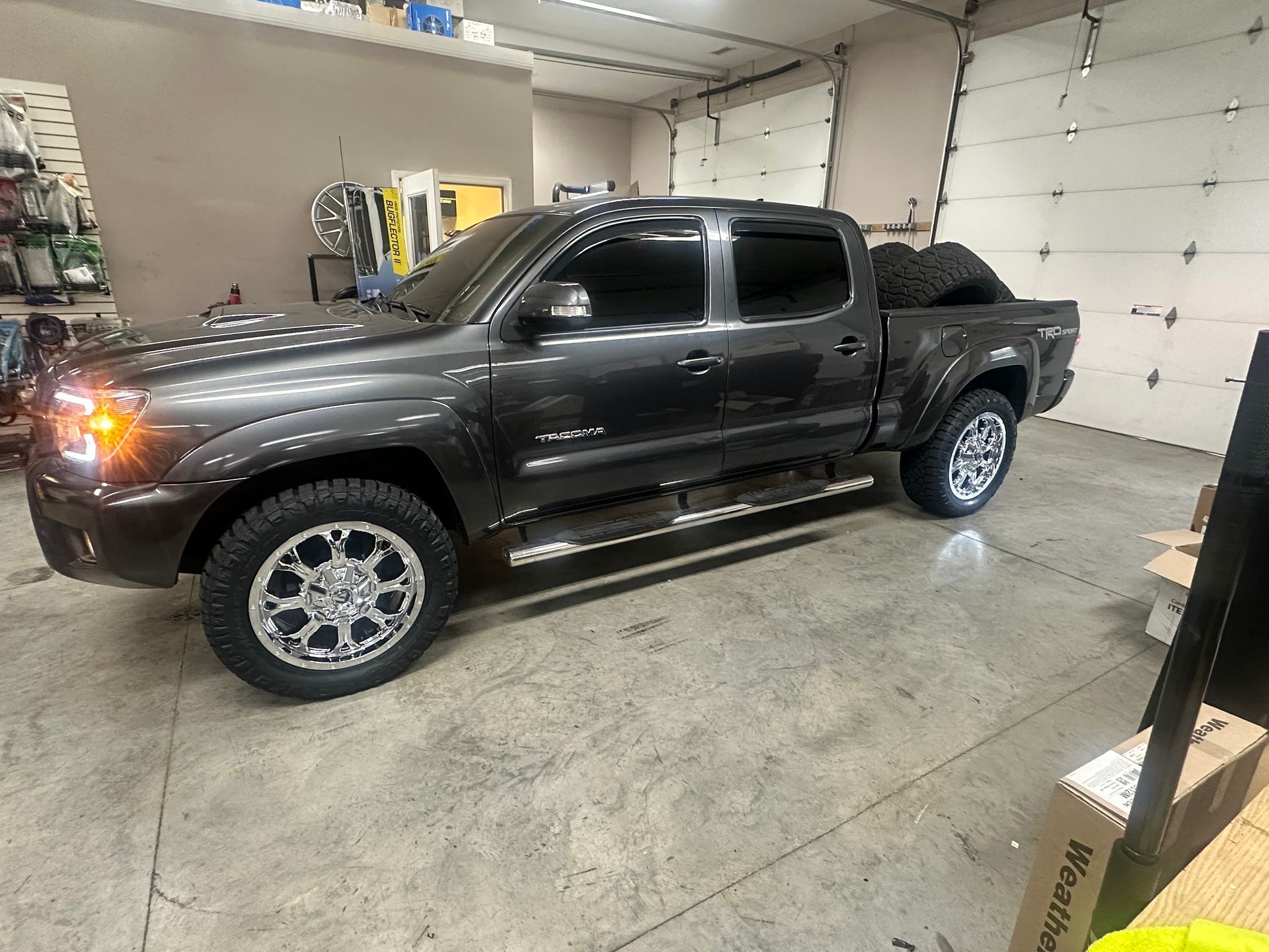 Dark grey Toyota Tacoma with new chrome wheels, parked inside a garage.
