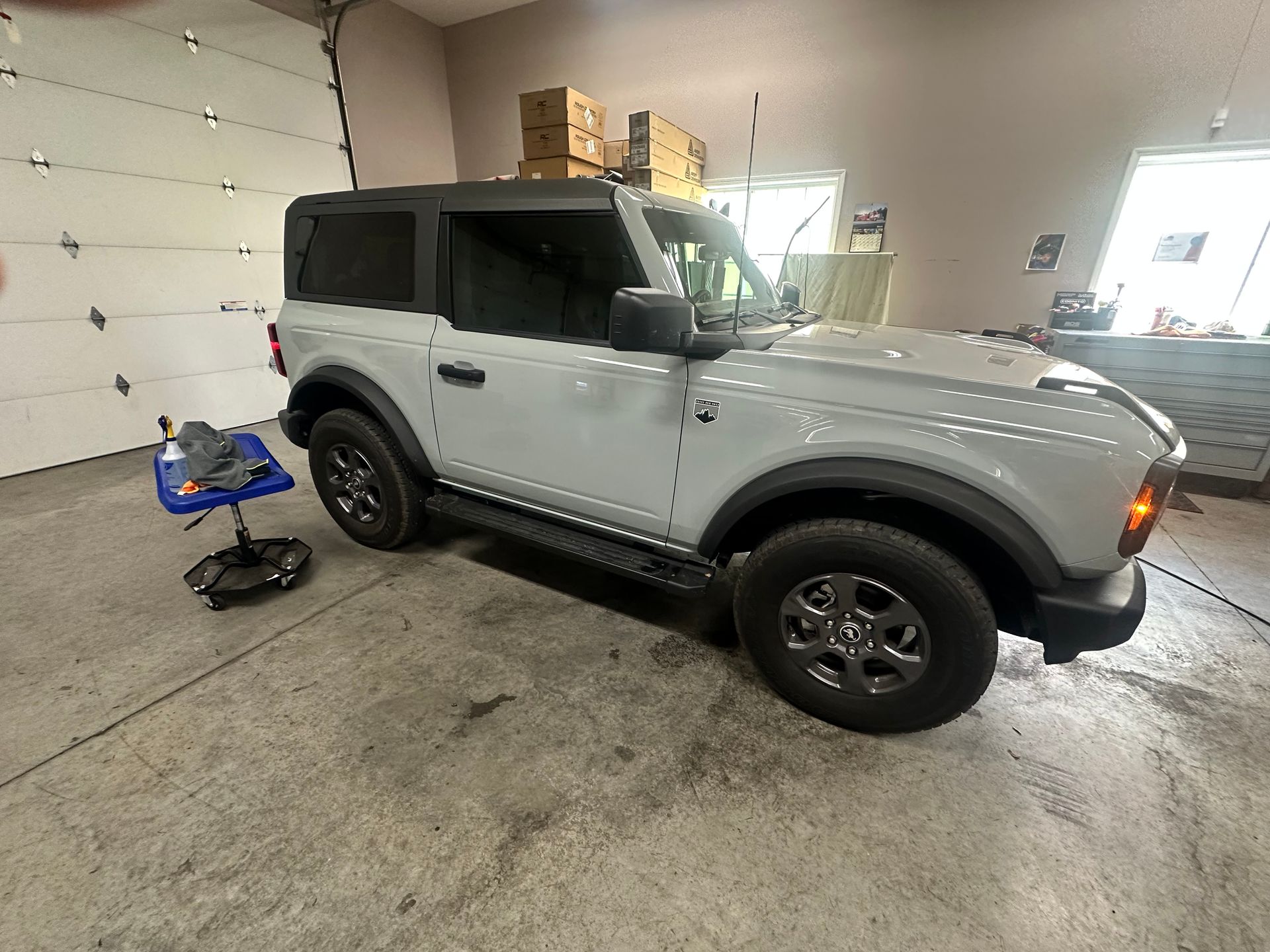 A light gray Ford Bronco in a garage with the garage door open.