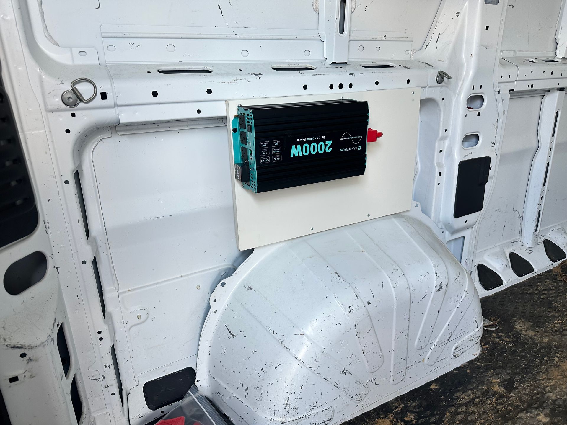 A black 2000W inverter mounted on a white panel inside a white van.
