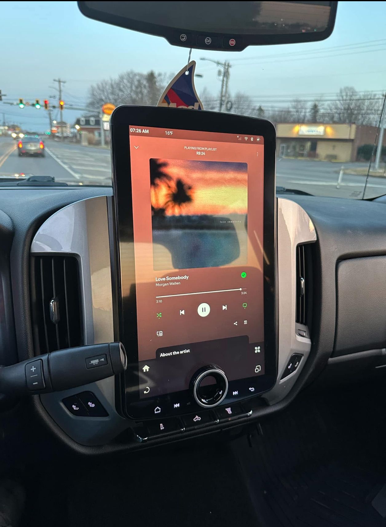 Tablet mounted on a car dashboard, displaying a sunset image and music controls.