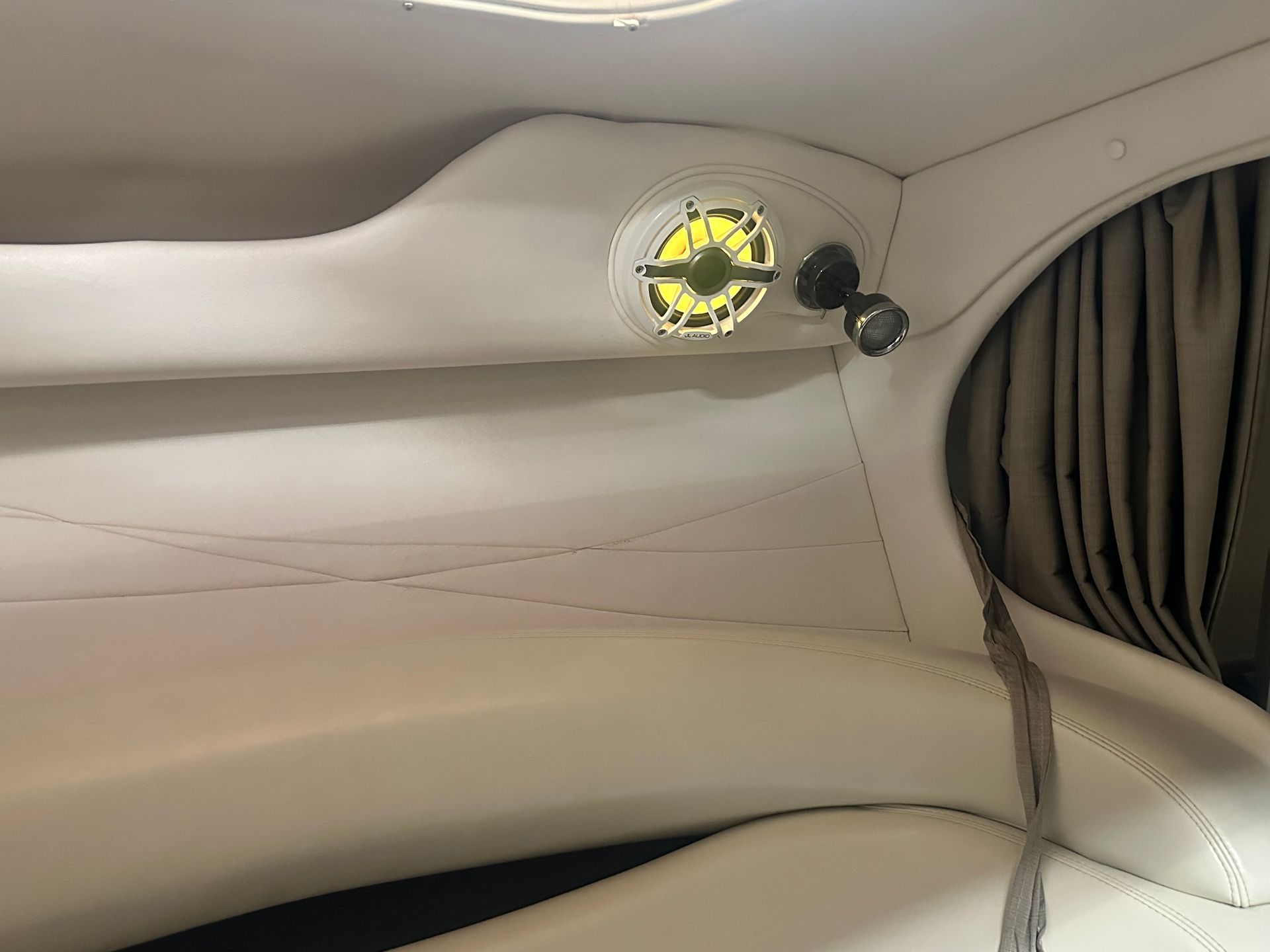 Cream-colored boat interior with speaker and spotlight near a window with tan curtains.