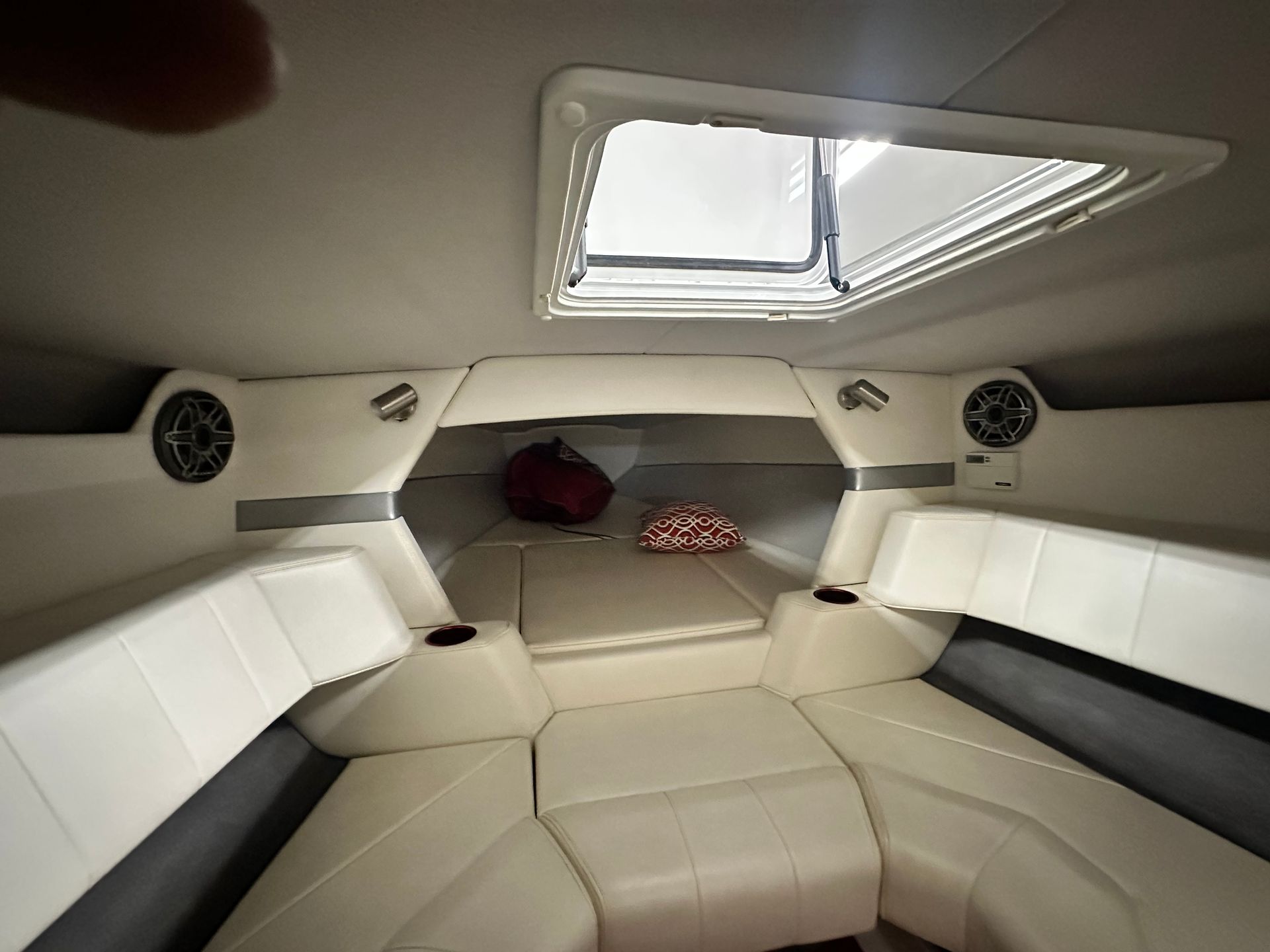 Interior of a boat cabin with white seating, overhead window, storage area, and speakers.