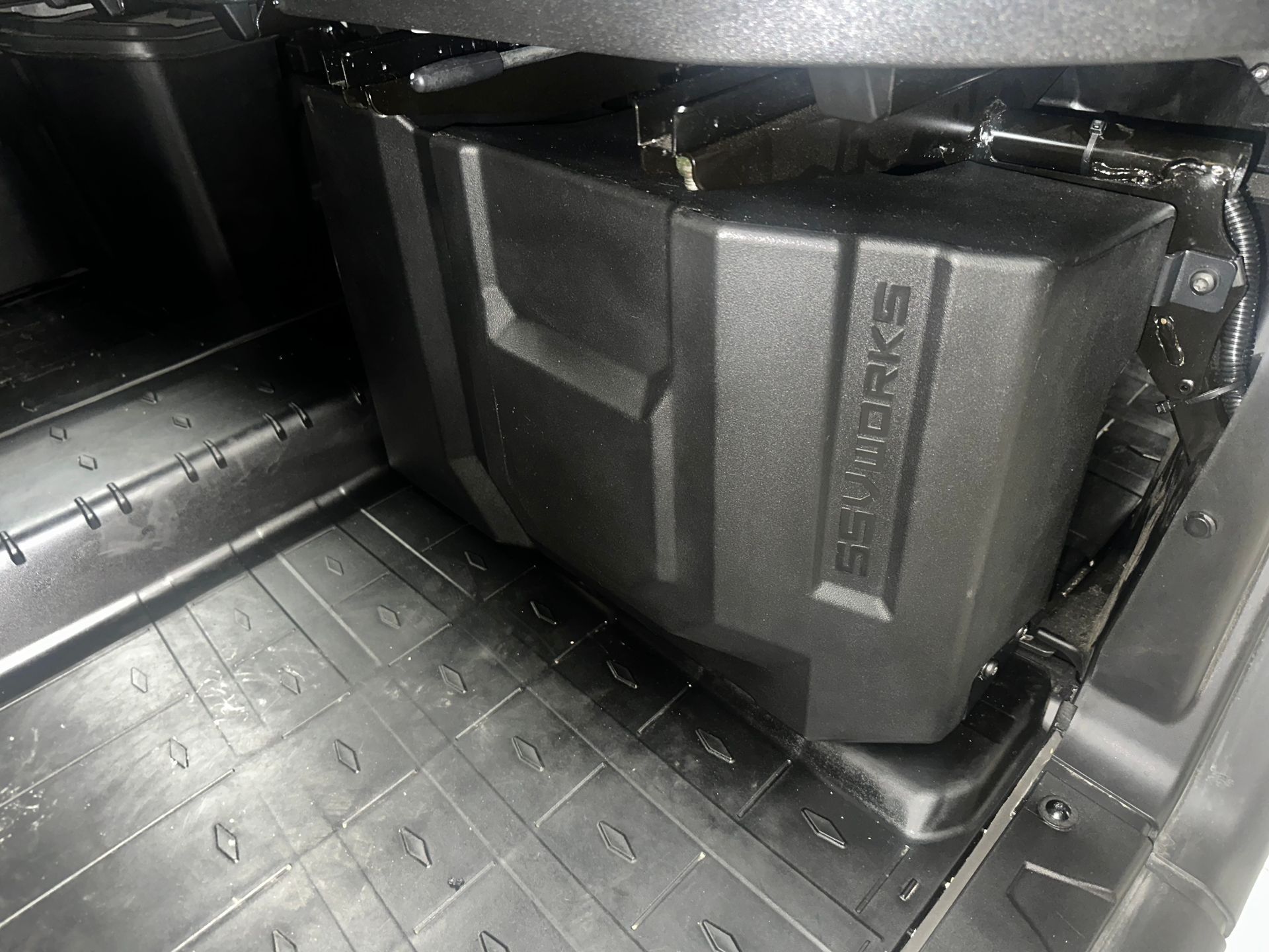 Black subwoofer box installed in a vehicle, against a plastic floor.