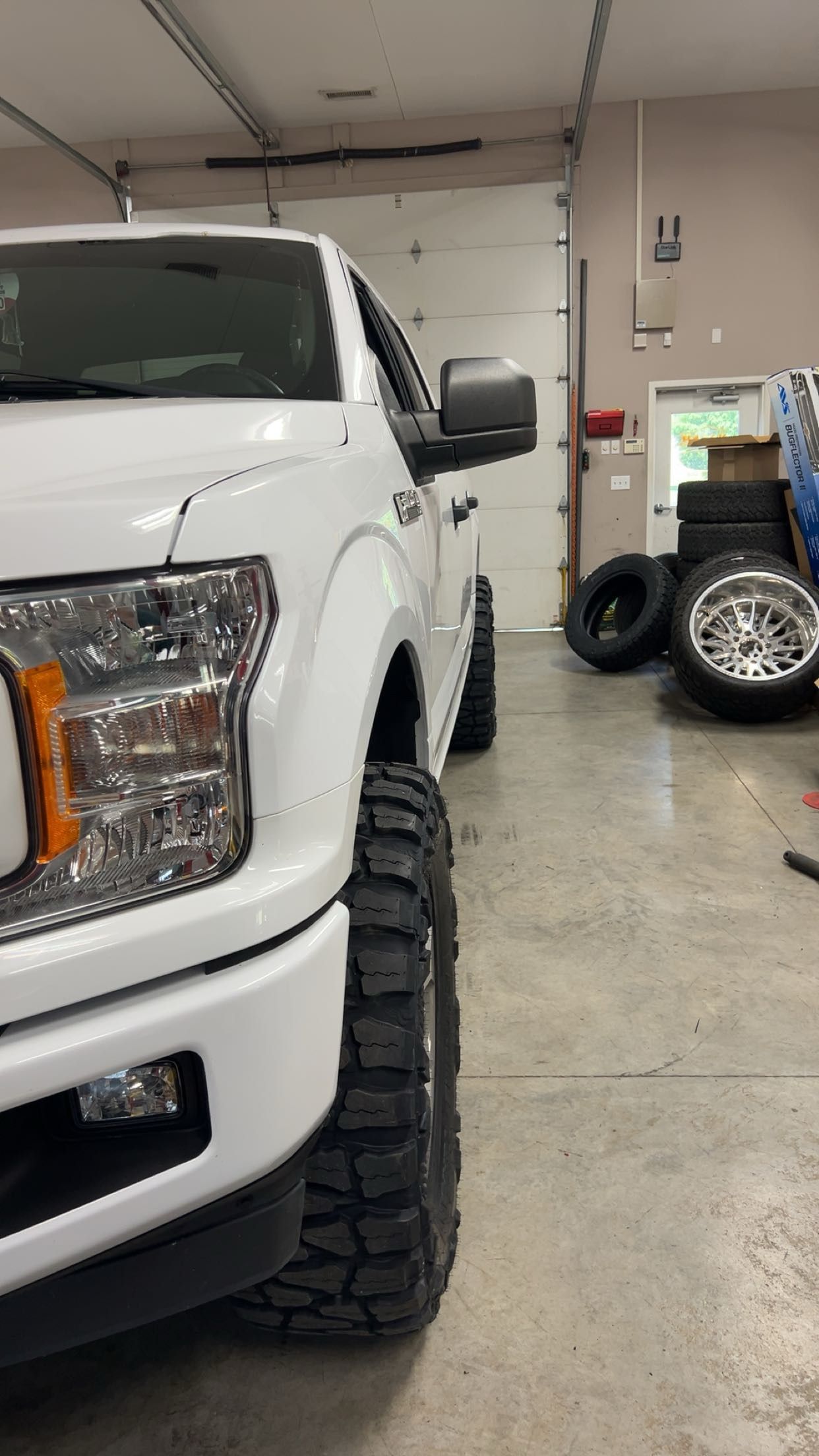 White Ford pickup truck with black off-road tires, parked inside a garage.