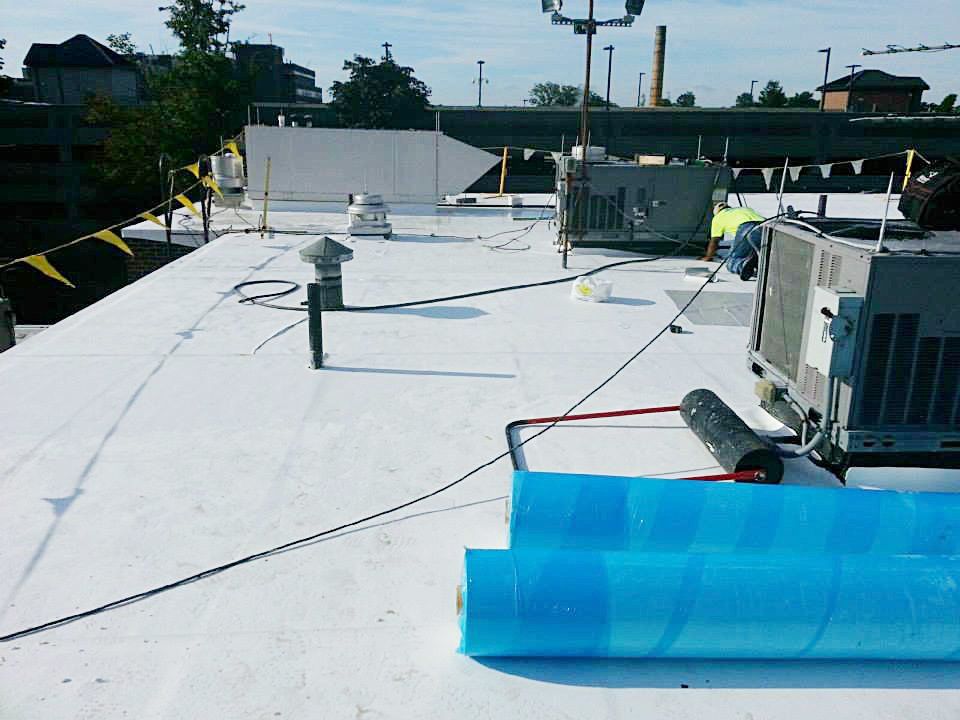 Flat commercial rooftop with white surface, equipment, and blue rolled materials.