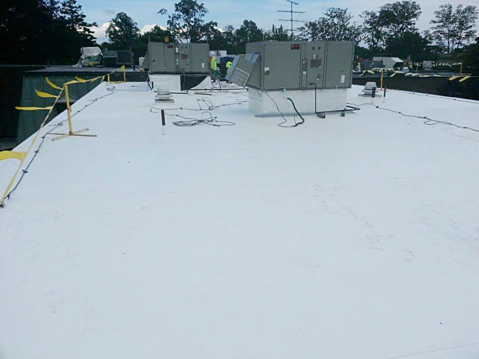White commercial roof with HVAC units; construction worker working on top.