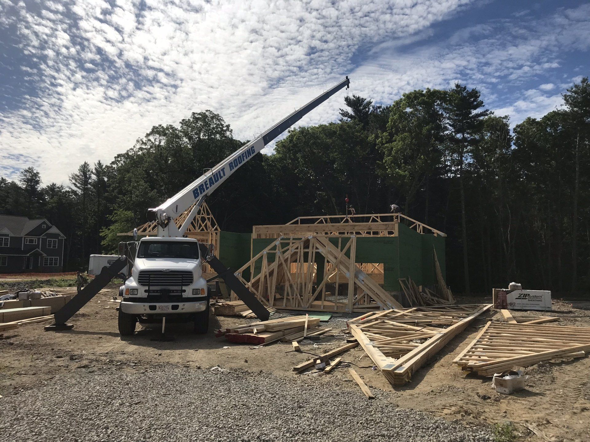 Construction site with a crane lifting wood framing for a house. White truck in the foreground. Sunny sky.