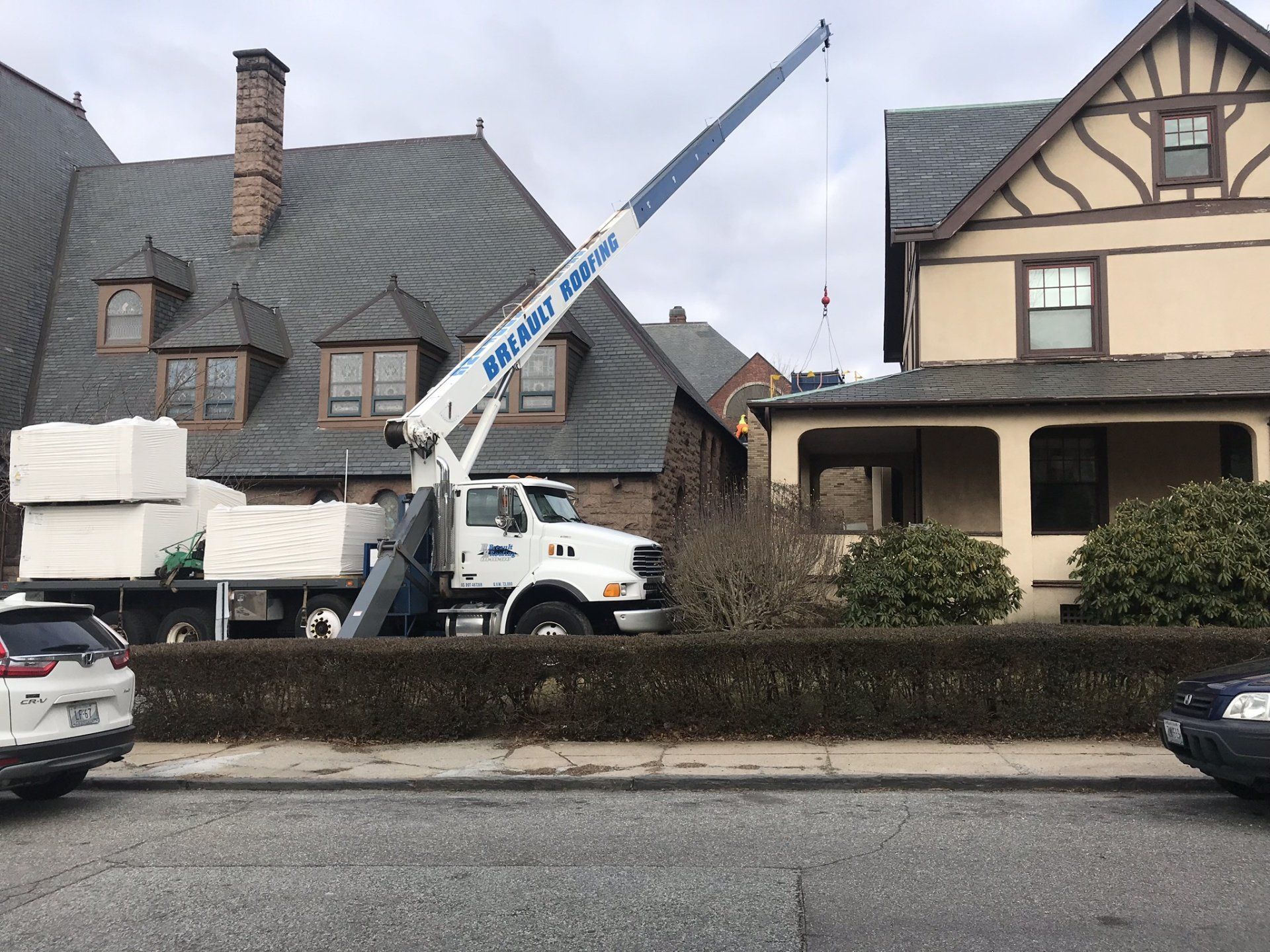 Crane truck lifting materials near houses on a street.