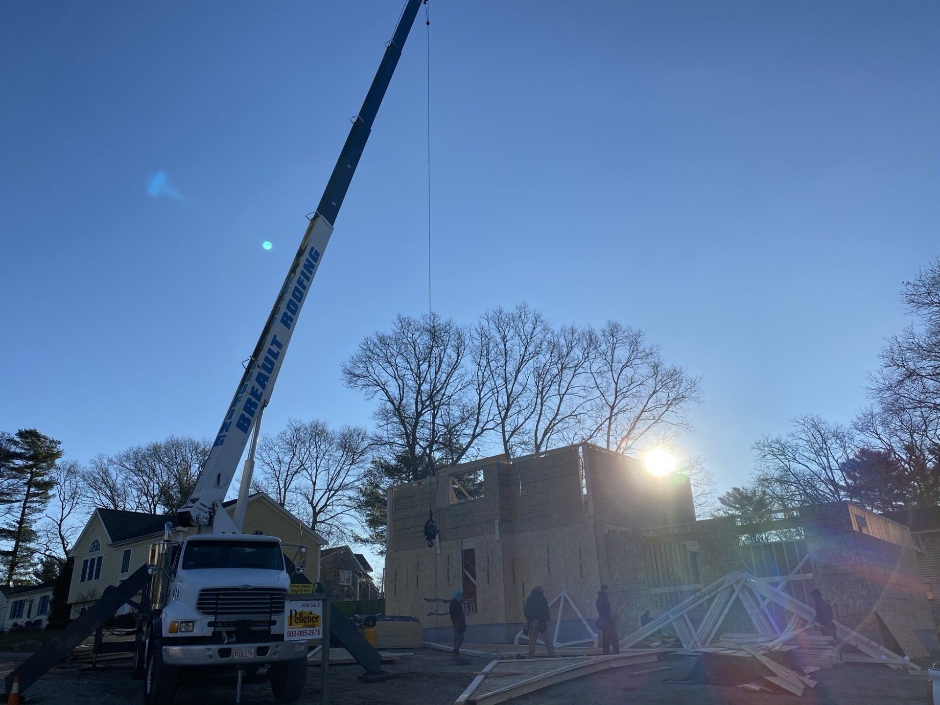Construction site with crane lifting lumber; workers building a house on a sunny day.