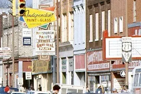 A street-level view of a small-town main street with storefront signs, including 
