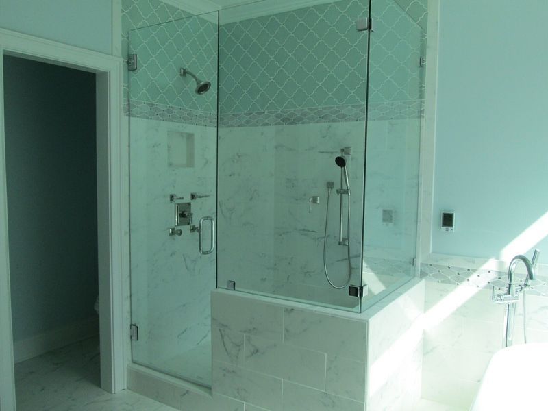A spacious bathroom with a glass-enclosed shower. The shower has marble tiling, a rain showerhead, and a hand-held shower.