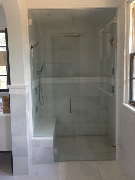 A walk-in shower with clear glass doors and walls, a built-in bench, and a rainfall showerhead. The shower is in a white-tiled bathroom.