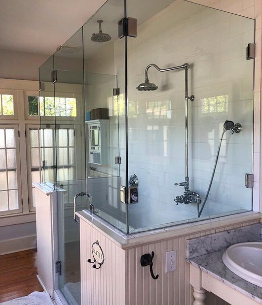 A modern bathroom with a glass shower enclosure and white beadboard. Chrome shower fixtures and a vanity with a marble countertop are also visible.
