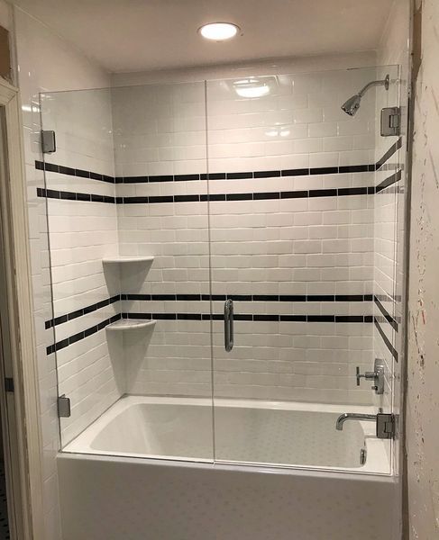 A newly renovated white bathroom with a glass shower door, white subway tiles with black stripes, and a built-in shelf.