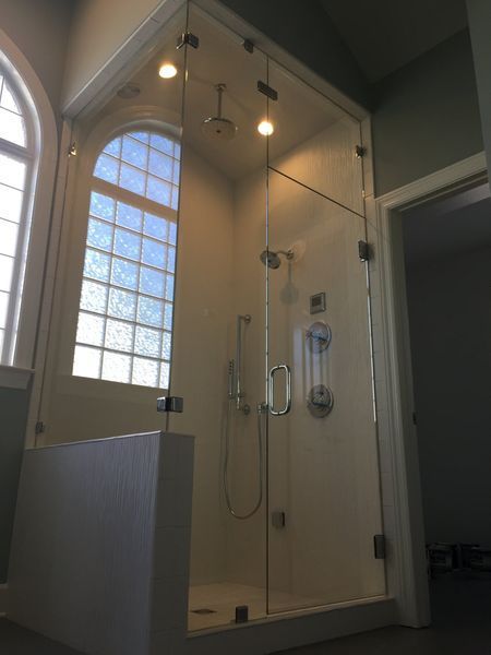 A modern glass shower enclosure with a rain shower head and handheld sprayer next to a tall arched window.