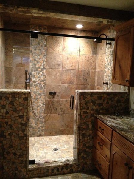 A bathroom with a stone-tiled shower and glass door. Brown cabinets are on the right, and a light shines from the ceiling.