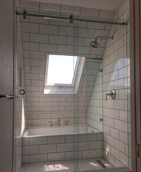 Small bathroom with a white tiled shower and bathtub, a window, and glass shower door.