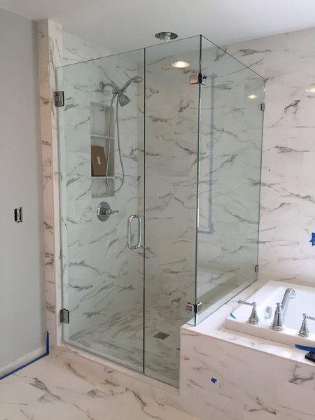 Glass shower enclosure with marble tile walls and floor, next to a white bathtub.