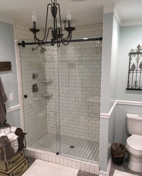 A bathroom with a glass shower, white subway tiles, a black chandelier, and light blue walls. A toilet and decorative wall piece are also visible.