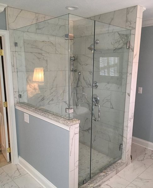Glass-enclosed corner shower with marble tile walls and a gray and white color scheme. A partial wall is visible on the left.