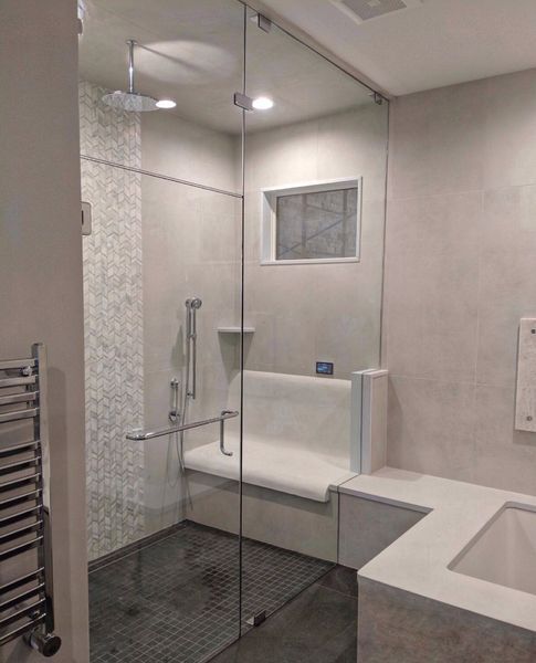 Modern accessible bathroom with a glass-enclosed shower, bench seating, and tiled walls.