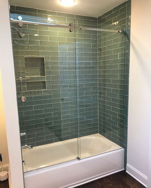 A modern bathroom with a white bathtub, teal subway tile, and a sliding glass shower door.