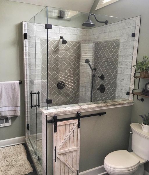 A modern shower with a glass enclosure, featuring a barn door, and grey tile accents. The shower is next to a white toilet in a bathroom.