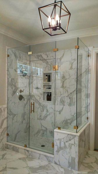 A modern marble-tiled shower with glass doors and gold fixtures, in a bathroom with a geometric chandelier.