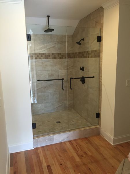 A modern glass shower with a stone tile interior, black hardware, and wooden floor.