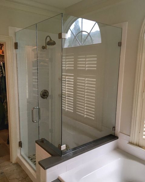 A glass shower enclosure in a bathroom with a view of shutters through the glass.