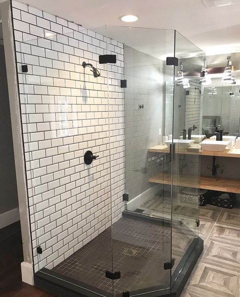 Modern shower with white subway tile, black fixtures, and glass doors. The shower has a dark floor and is adjacent to a vanity with two sinks.