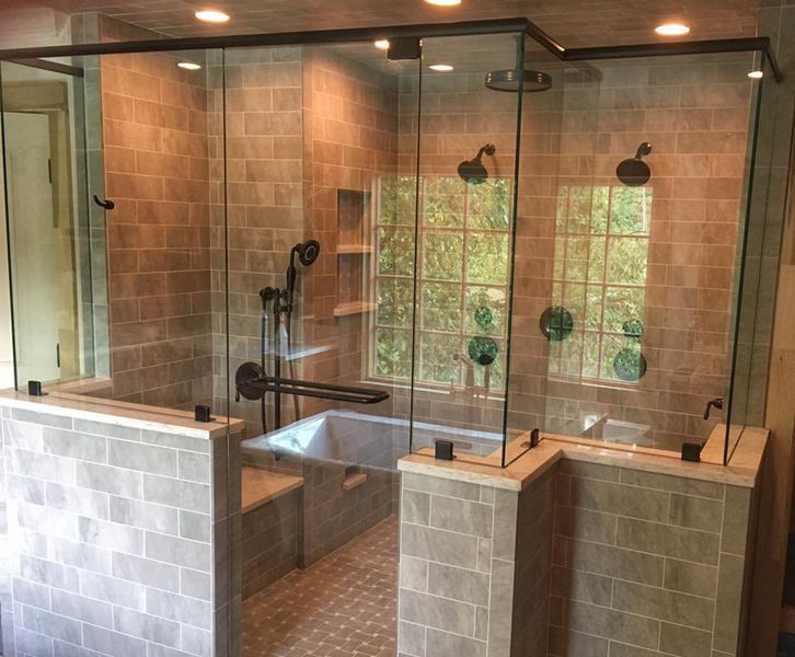 A luxurious bathroom featuring a large glass-enclosed shower with two shower heads, a built-in tub, and gray tile walls.